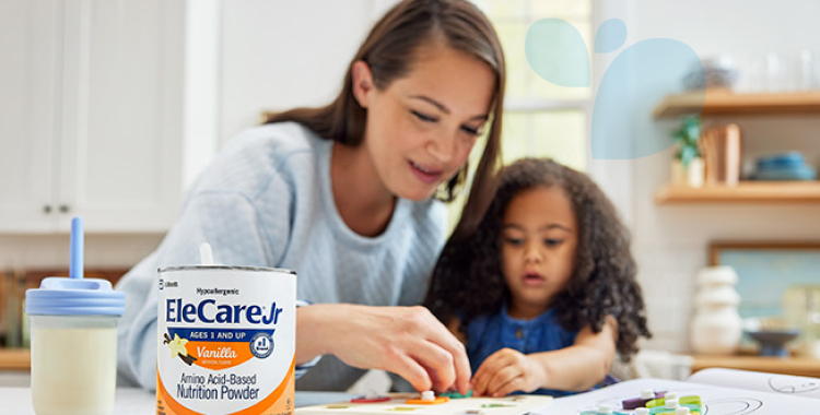 Mom and young daughter playing a puzzle game at the kitchen island. A sippy cup and can of EleCare Jr Vanilla are in front of them.