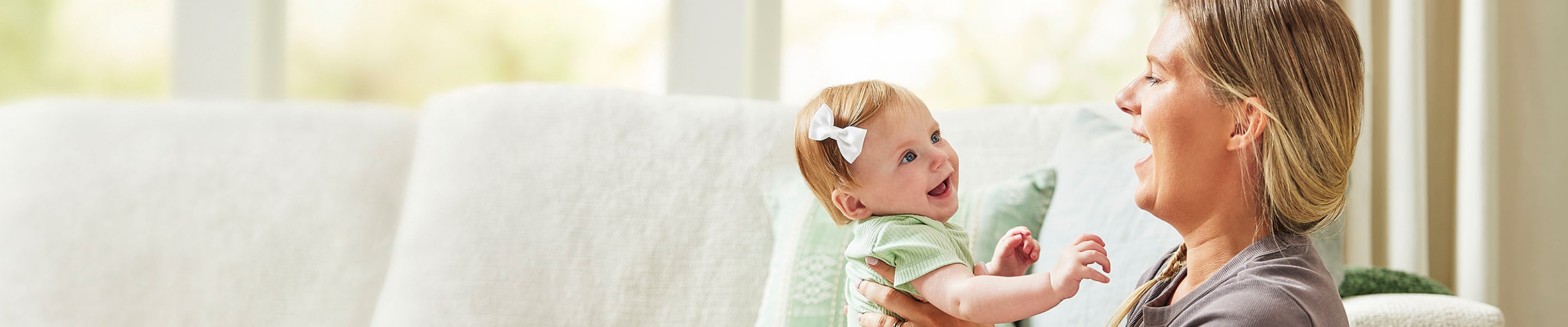 Woman in front of couch in living room, holding baby girl up; both are smiling at each other.