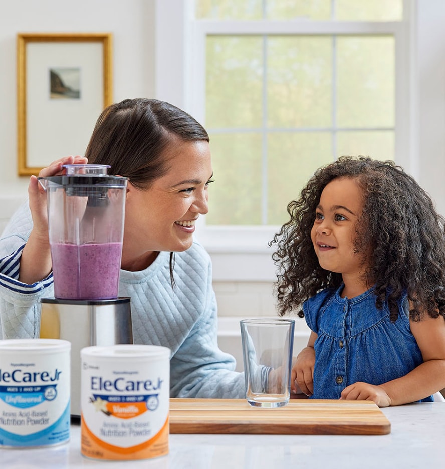 Woman in kitchen making a purple smoothie in a blender using EleCare Jr. Young girl watching and waiting for the smoothie.